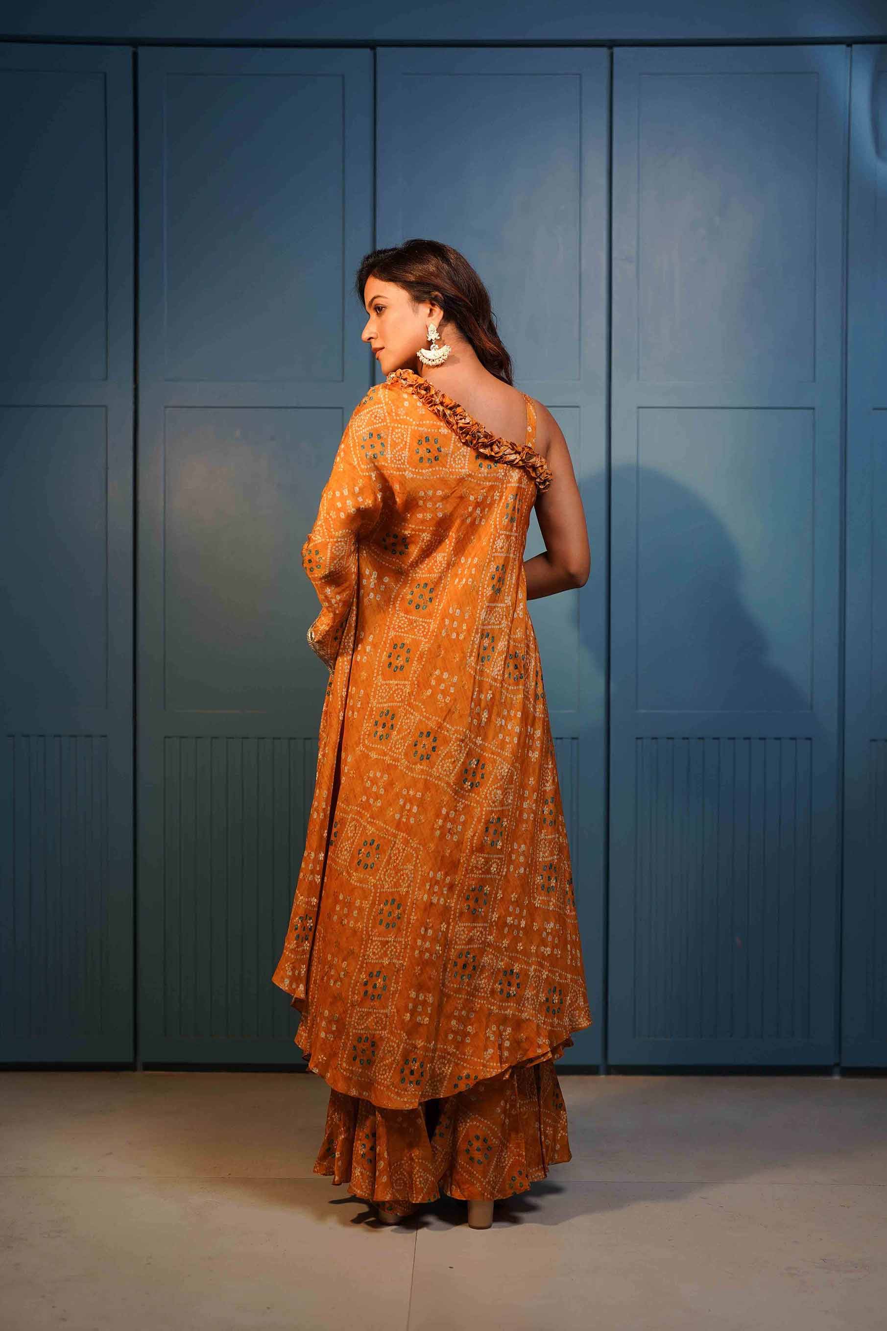 Rust yellow one shoulder tunic with ruffles paired with ruffled gharara..
