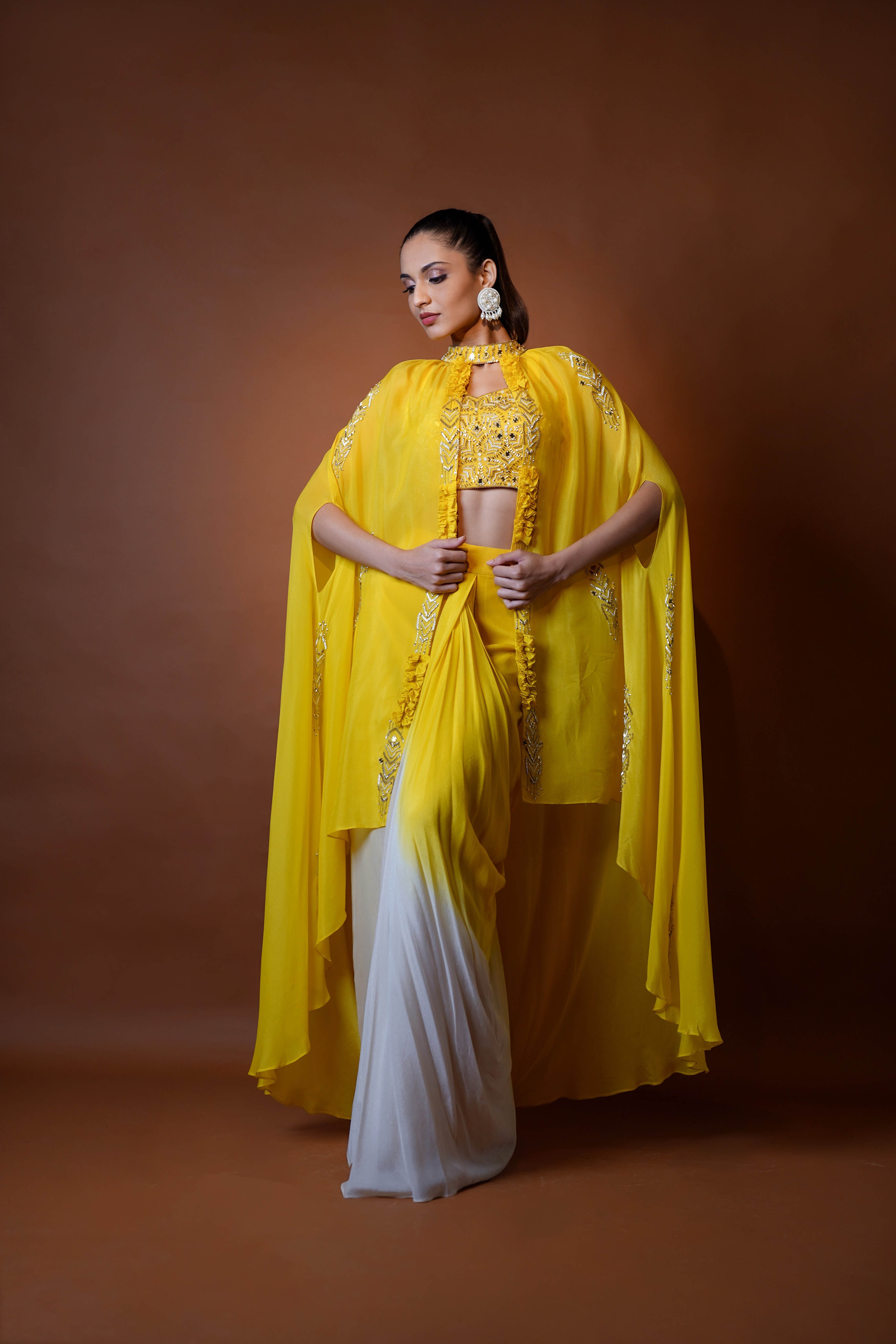 Mustard yellow cape jacket with crop top and draped shaded skirt.