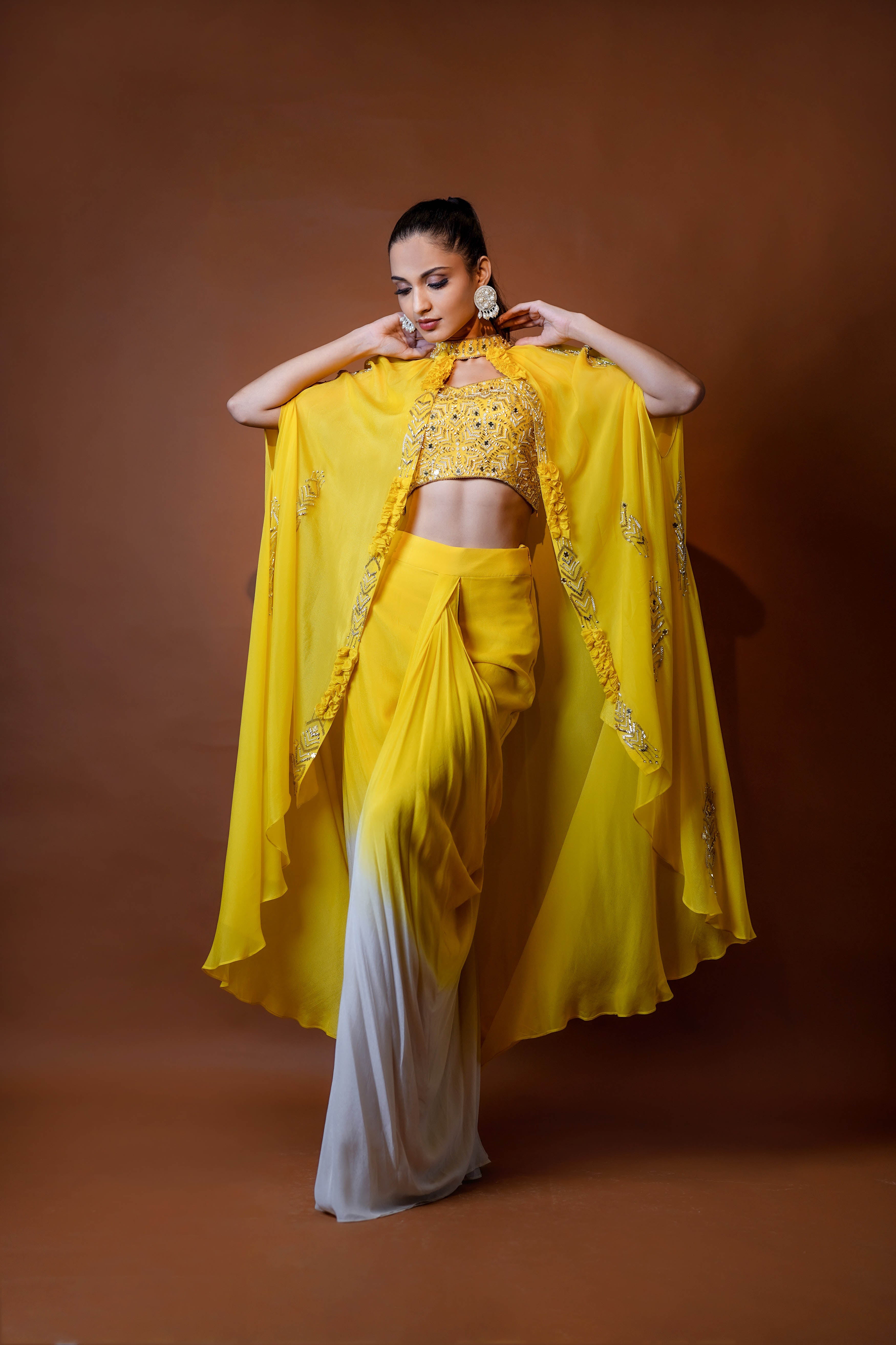 Mustard yellow cape jacket with crop top and draped shaded skirt.
